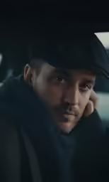 a man sitting in a car with a hat on