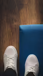 a person wearing white sneakers and standing next to a blue mat