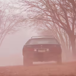 the car is driving down the road in the dust