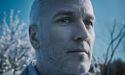 a man with white hair stares directly at the camera