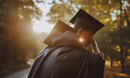 a male student in graduation gown is outside and talks on a cellphone