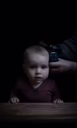a little baby in a brown shirt holding a camera