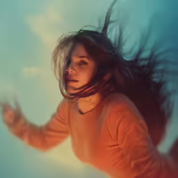 a woman in orange top with hair blowing in wind