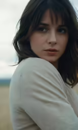 a woman with long brown hair is wearing a white shirt and is looking at the camera