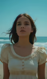 a woman in white dress standing on beach by ocean