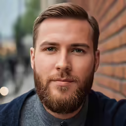 a man with brown hair and beard standing next to a brick wall