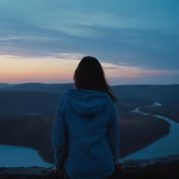 a young girl stands at the peak watching the sunset