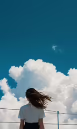 a woman is standing in front of a fence with her hair blowing in the wind