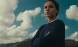 a woman standing with her arms crossed in front of a beautiful sky