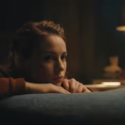 young woman staring into distance at night in dimly lit room