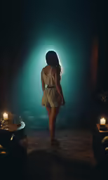 a young woman in a short dress standing on a dark background, with lit candles at her feet