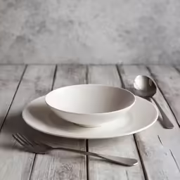 two white bowls and a spoon are set next to each other on a wooden table