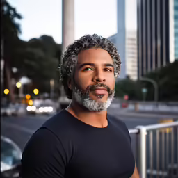 an african man wearing a black t - shirt in front of a street and buildings