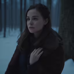 a girl wearing a coat standing in front of some trees