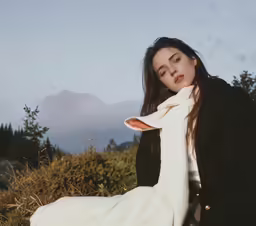 a woman in a long dress and coat on a hill