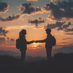 two people with backpacks shake hands at sunset