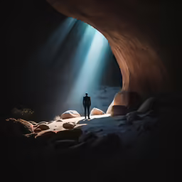 man standing at the entrance of a cave looking into the light