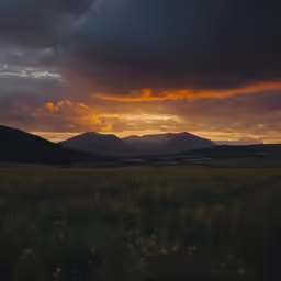 an open field with mountains and clouds in the distance