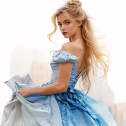 a woman in a blue dress poses by a white wall