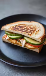 a grilled cheese and cucumber sandwich sitting on a black plate