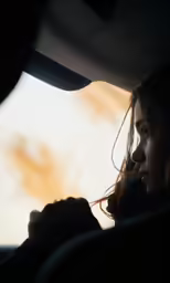 a woman driving a car while sun sets behind her
