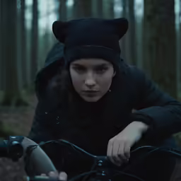 the girl in the black coat rides a bike through the forest