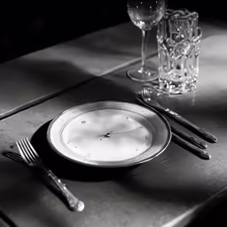 a black and white photo of a clock on a table with two forks, one in the middle