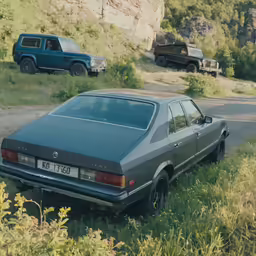 an old car is parked in a field beside a cliff