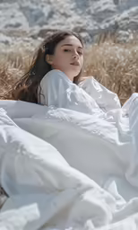 a beautiful woman is laying down in a white blanket