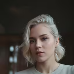 a woman with blonde hair and earrings looks at the camera