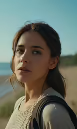 a young woman stands on the beach with a serious expression