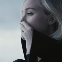 a woman wearing black is rubbing her nose with her hand