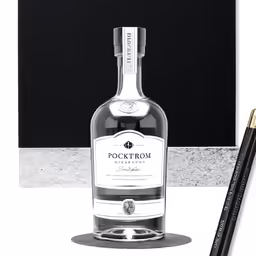a bottle of whisky and a single black ink pen sit next to a glass