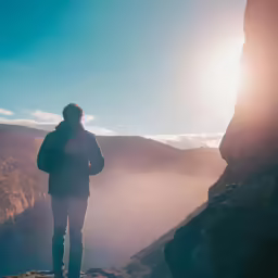 a man standing at the edge of a cliff looking at the sun