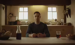 man sitting in the kitchen while he has a glass