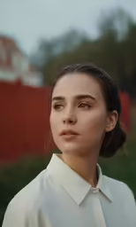 a woman with dark hair stands outside in a white blouse