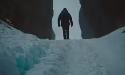 man walking into dark snowy cave with light at end