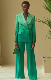 a woman wearing green pants and a suit,an african american woman is standing with a green suit and purse