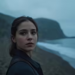 a young woman stands on the edge of a beach