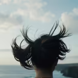 a woman with her hair in a messy top bun stands on a pier overlooking the ocean