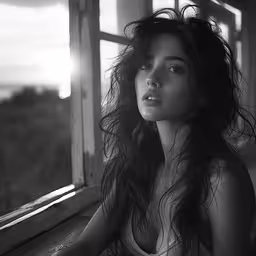 a black and white image of a woman looking out the window,a beautiful young lady is looking out a window