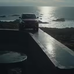 an orange car driving on a road beside the ocean