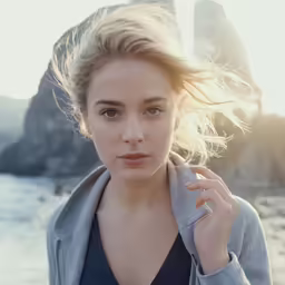 a woman with blond hair stands near the ocean