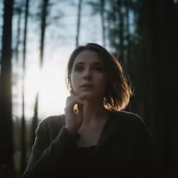 the woman stands among the trees in a grove of dark trees