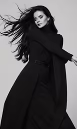 the model poses in black, draped coat and pants