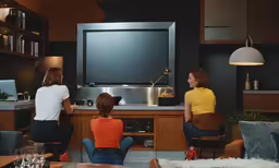 two women watch a television in the living room while three other women sit in chairs