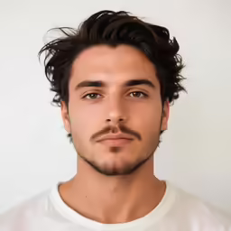 man with curly hair and mustache looking into camera