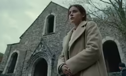 a girl wearing a coat in front of a building