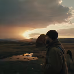 a man standing in front of a mountain near a body of water