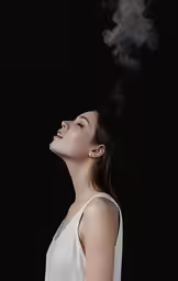 a woman looks upward in front of a smokey substance floating from her mouth